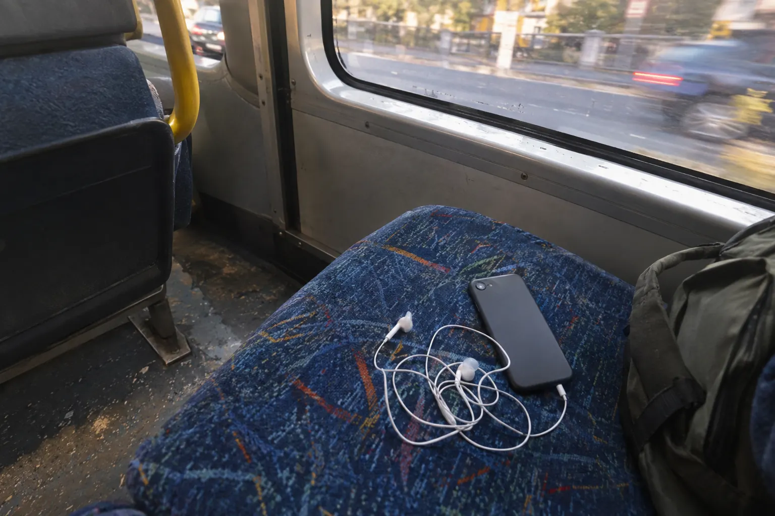 Wired earphones and a smartphone lying on a worn bus seat by the window during a morning commute