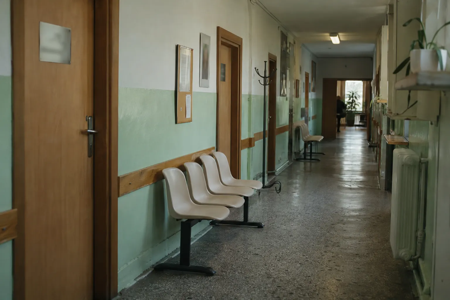 Коридор польської поліклініки: пластикові стільці вздовж стіни, двері кабінетів і вішак для одягу
