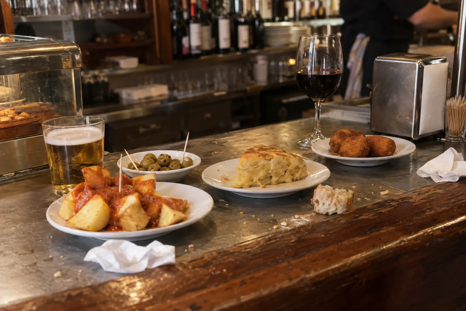 Bar tapas w Hiszpanii: patatas bravas, oliwki, tortilla i krokiety na kontuarze obok piwa i wina